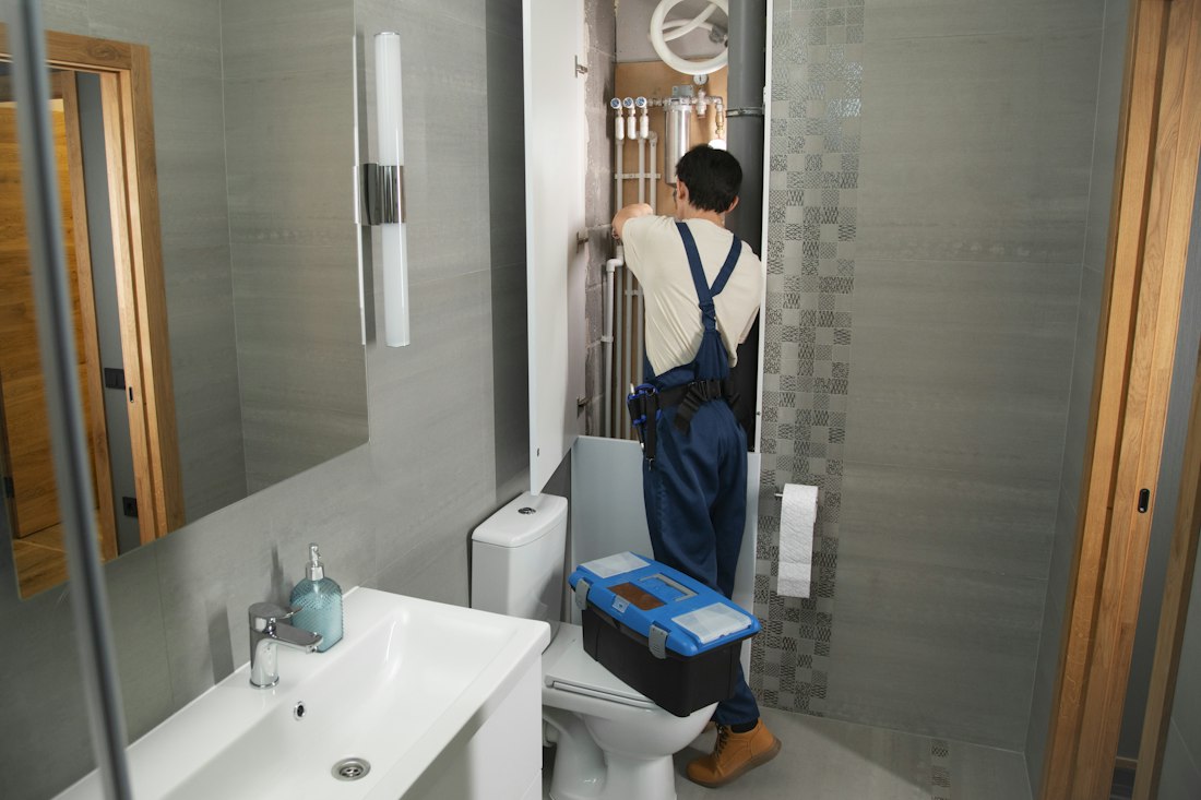 Plombier intervenant sur les arrivées d'eau d'une salle de bains